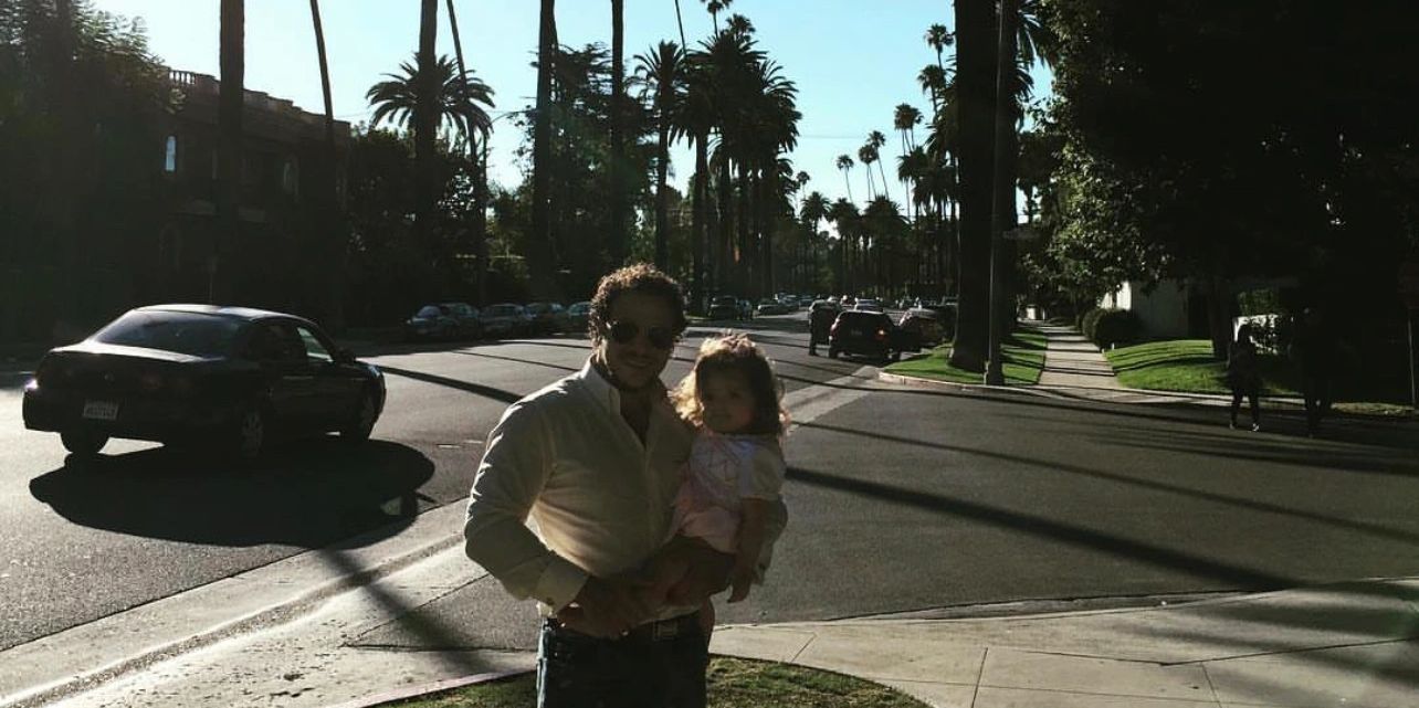 Man holding a child on a sunny street lined with palm trees.